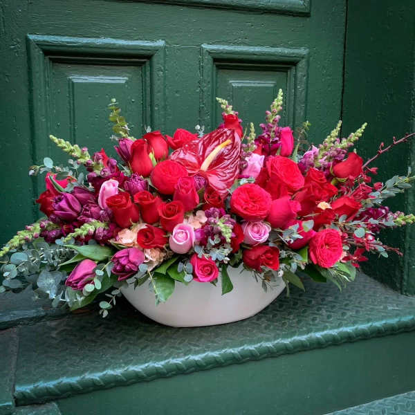 Low floral arrangement of red and pink roses in a white bowl vase