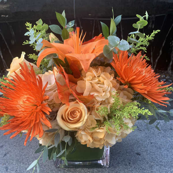 Orange and peach floral arrangement in a clear square vase