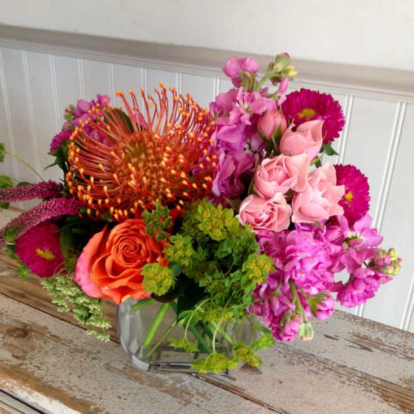 Mixed bouquet of pink, orange, and purple flowers in a clear glass vase