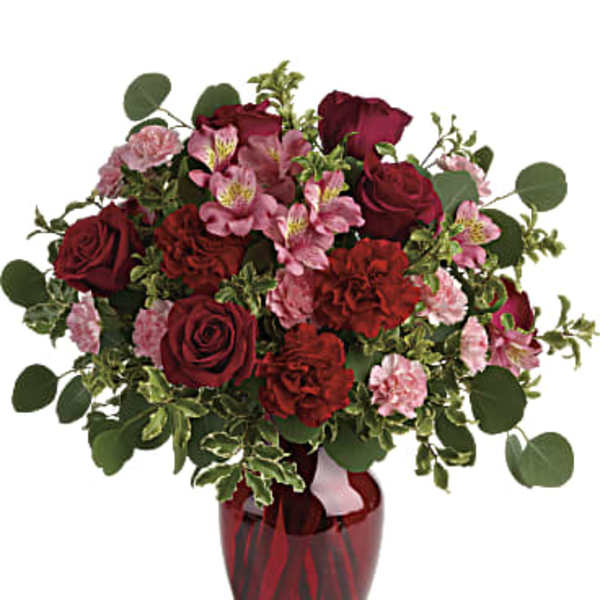 Bouquet of red roses and pink flowers in a red glass vase