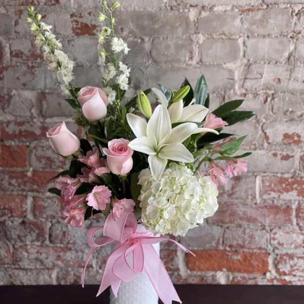 Pink roses and white lilies in a white vase with a pink ribbon