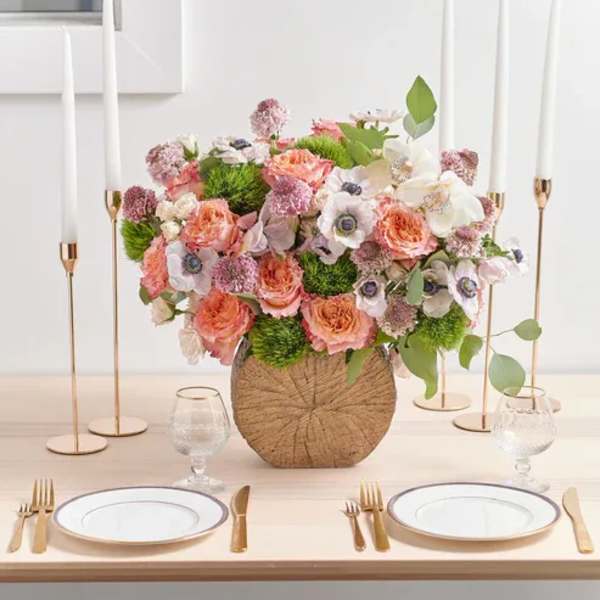 Pink and white floral centerpiece in a round woven vase on a table