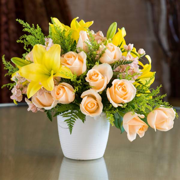 Peach roses and yellow lilies in a white vase