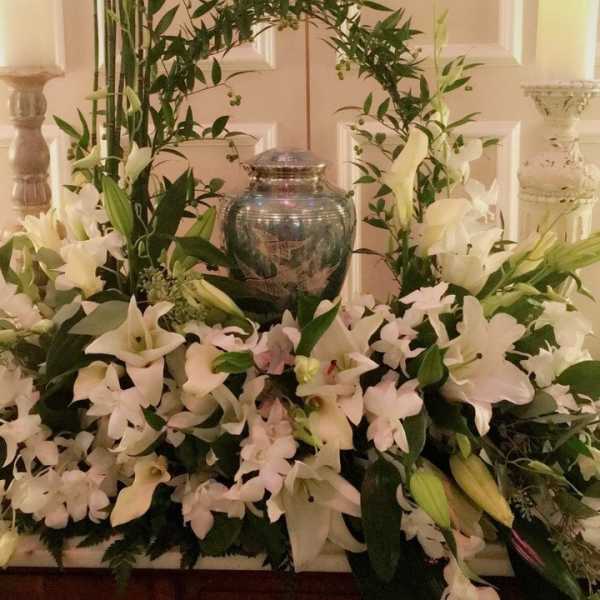 White floral arrangement with lilies and orchids around a silver urn