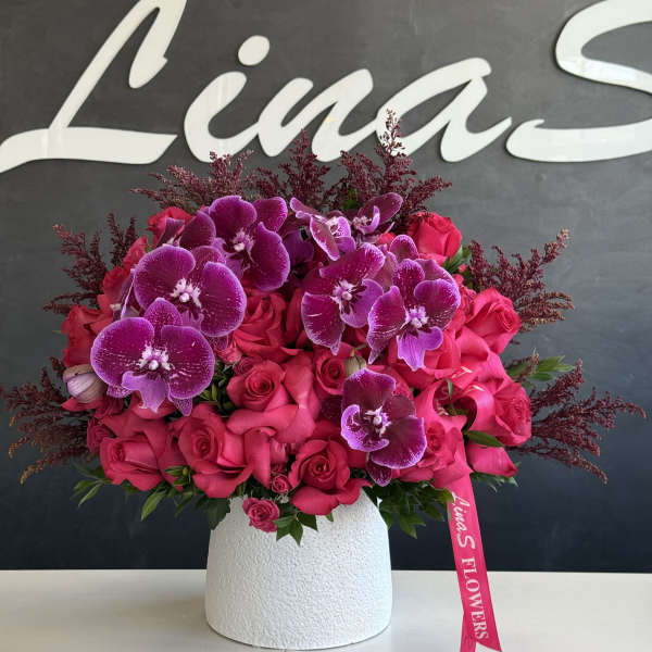 Pink roses and purple orchids arranged in a white vase