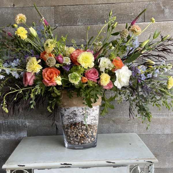 Large mixed floral arrangement in a clear vase with pebbles