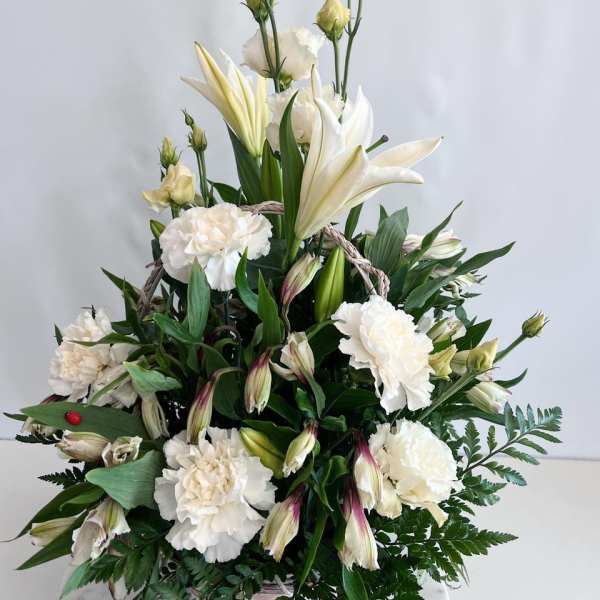 White lilies and carnations arranged in a basket with greenery