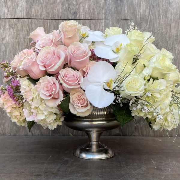 Pink and white roses with orchids in a silver pedestal vase