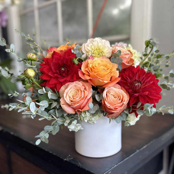 Bouquet of red, peach, and orange flowers in a white vase