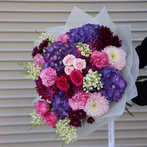 Hand-tied bouquet of pink, purple, and burgundy flowers wrapped in white paper