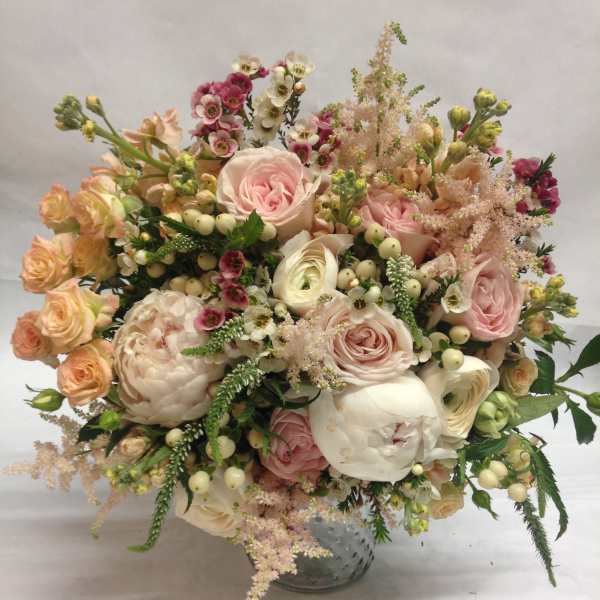 Blush and cream bouquet of roses, peonies, and small filler flowers in a glass vase.