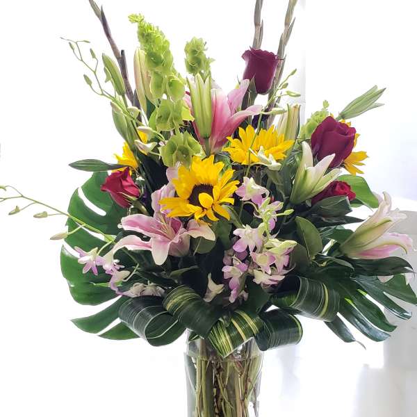 Tall mixed bouquet in a clear glass vase with lilies, roses, and sunflowers