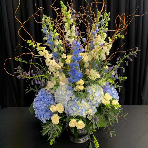 Tall blue and white floral arrangement in a black vase with curly branches