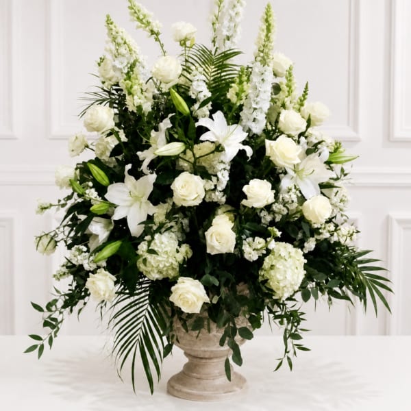 White floral arrangement with roses and lilies in a stone pedestal vase