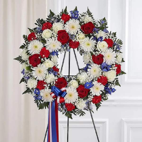 Red, white, and blue funeral wreath on a black stand with ribbon