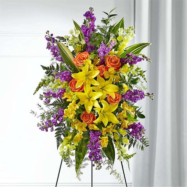 Standing floral spray with orange roses, yellow lilies, and purple flowers