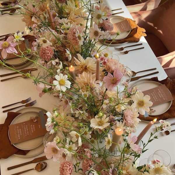 Pastel floral centerpiece running down a set table with candles and place settings