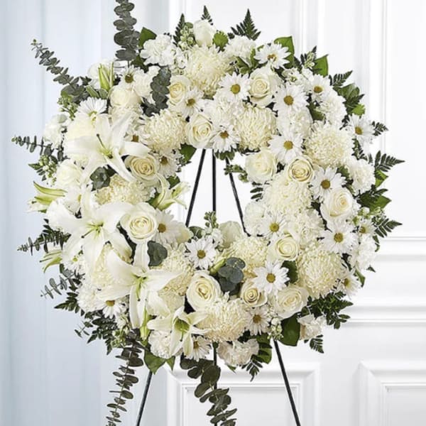 White funeral wreath on a black stand with roses, daisies, and lilies