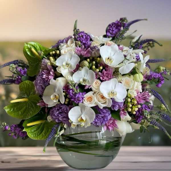 Purple and white floral arrangement in a glass bowl vase