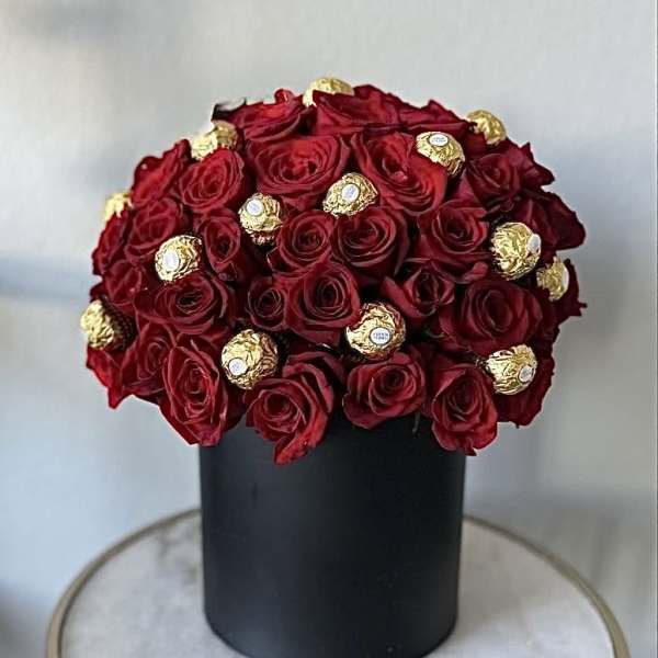 Red roses arranged with gold-wrapped chocolates in a black box