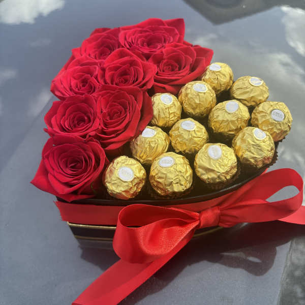 Red roses arranged with gold-wrapped chocolates in a heart-shaped box