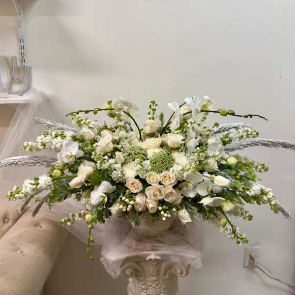 Large white floral arrangement with roses and orchids in a pedestal vase