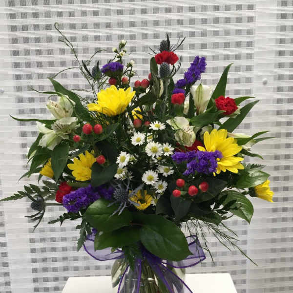 Mixed bouquet in a clear glass vase with yellow, purple, red, and white flowers