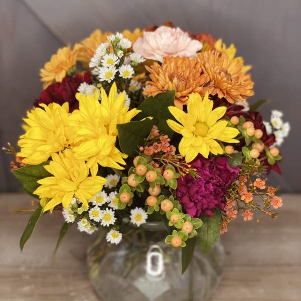 Mixed bouquet of yellow, orange, pink, and white flowers in a clear glass vase