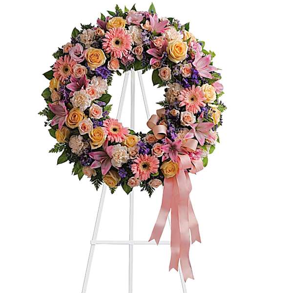 Pink and peach floral wreath on a white stand with a ribbon bow