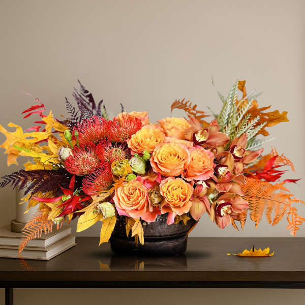 Orange roses and orchids in a dark vase with autumn leaves