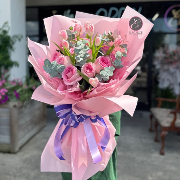 Pink rose and tulip bouquet wrapped in pink paper with a purple ribbon