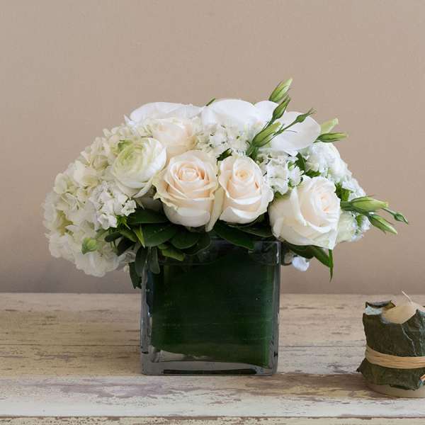 White roses and hydrangeas arranged in a square glass vase.