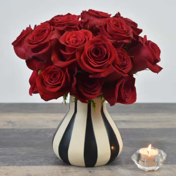 Red rose bouquet in a striped vase beside a lit candle