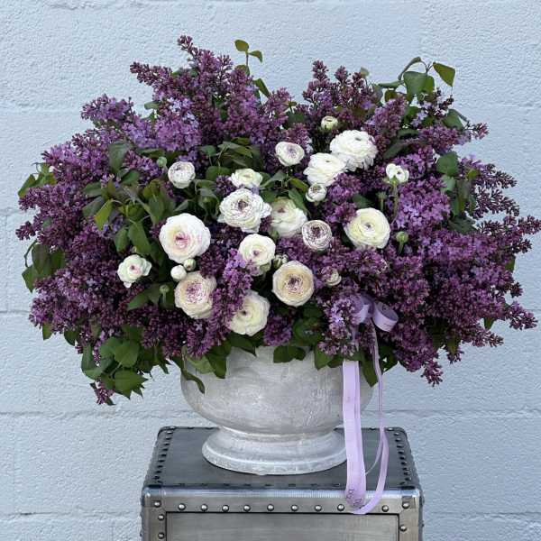 Large purple and white floral arrangement in a gray urn vase