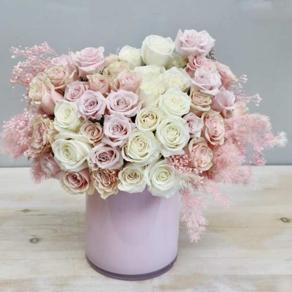 Round arrangement of pale pink and cream roses in a glossy light pink cylinder vase