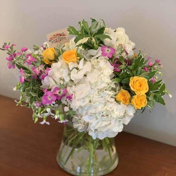 White hydrangeas with yellow roses and pink flowers in a glass vase