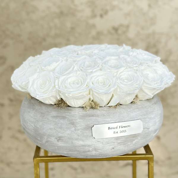 White roses arranged in a round gray box on a gold stand