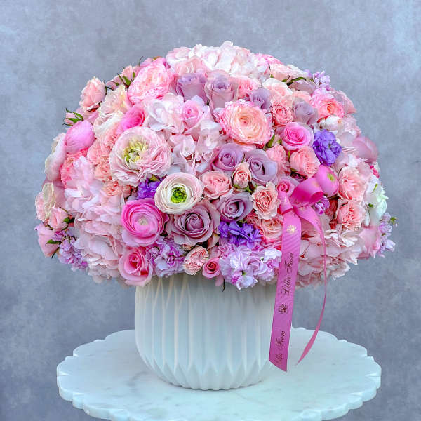 Large pink and lavender bouquet in a white vase with a ribbon