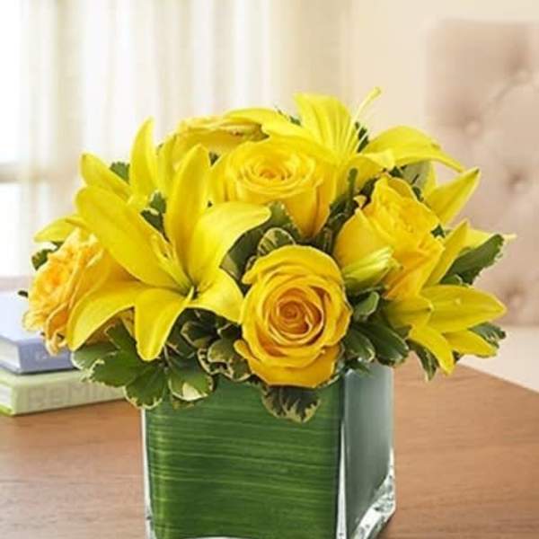 Yellow roses and lilies arranged in a square glass vase