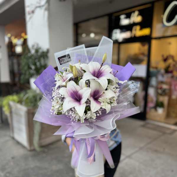 Bouquet of white lilies with purple centers wrapped in lavender paper