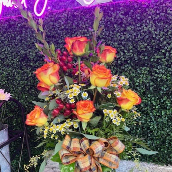 Tall bouquet of orange-yellow roses in a glass vase with a plaid ribbon