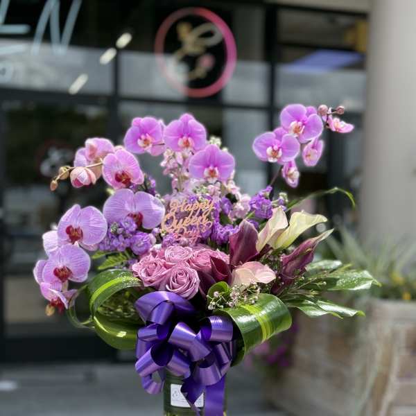 Purple orchid and rose bouquet in a glass vase with a ribbon
