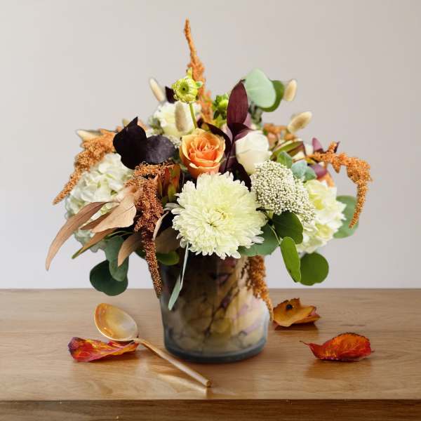 Mixed floral arrangement in a glass vase with an orange rose and white blooms