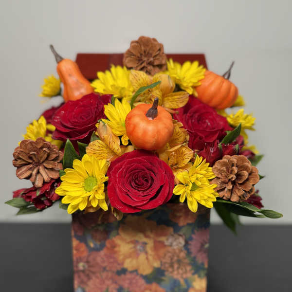 Bouquet of red roses and yellow daisies in a floral box with small pumpkins