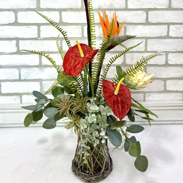 Tropical arrangement with bird of paradise, red anthuriums, and a woven vase