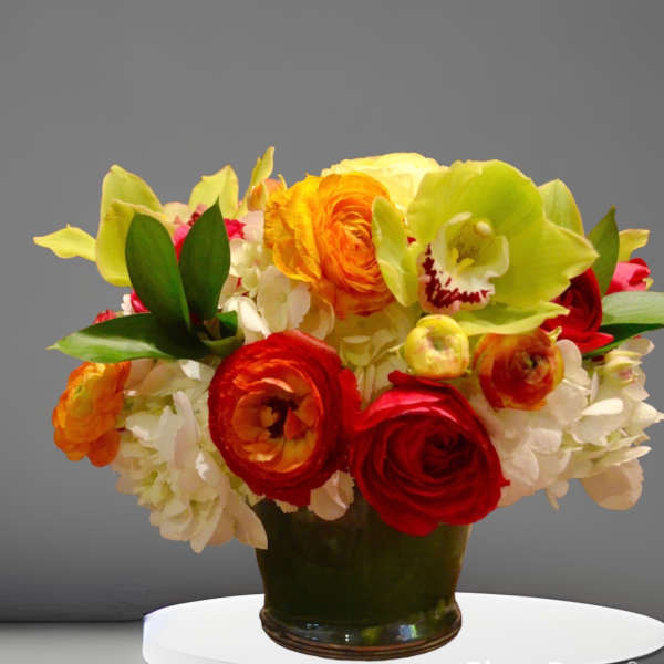 Colorful bouquet of ranunculus, orchids, and hydrangeas in a dark vase
