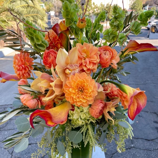 Orange floral arrangement with calla lilies, orchids, and dahlias in a glass vase
