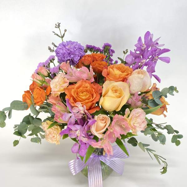 Mixed bouquet of orange, pink, and purple flowers in a glass vase