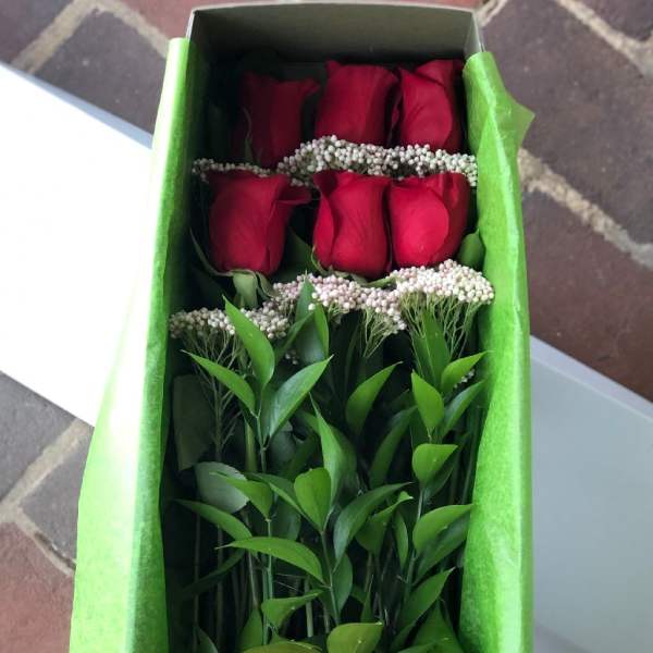 Boxed arrangement of long-stem red roses with a red satin bow in green tissue paper