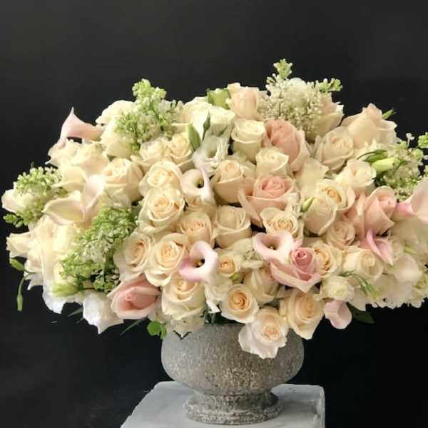 Large bouquet of cream and blush roses with calla lilies in a stone vase